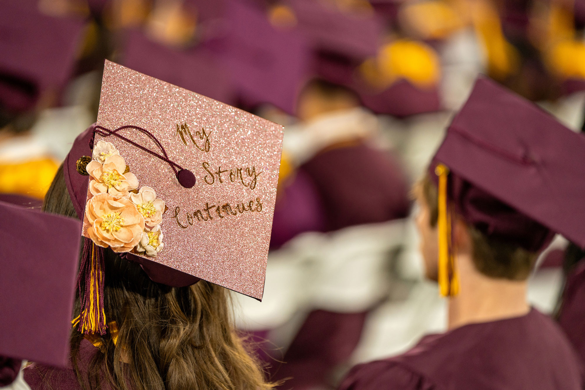 Convocation with a hat in focus reading “My Story Continues”.